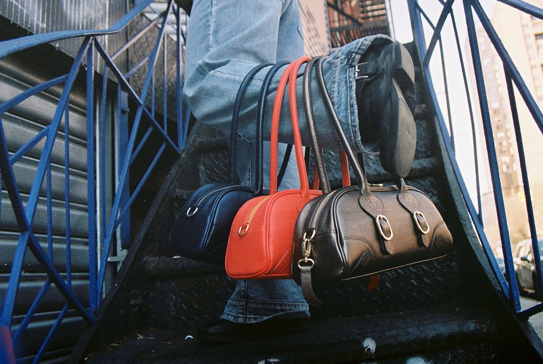 The SS26 collection — four bags resting on a city stoop
